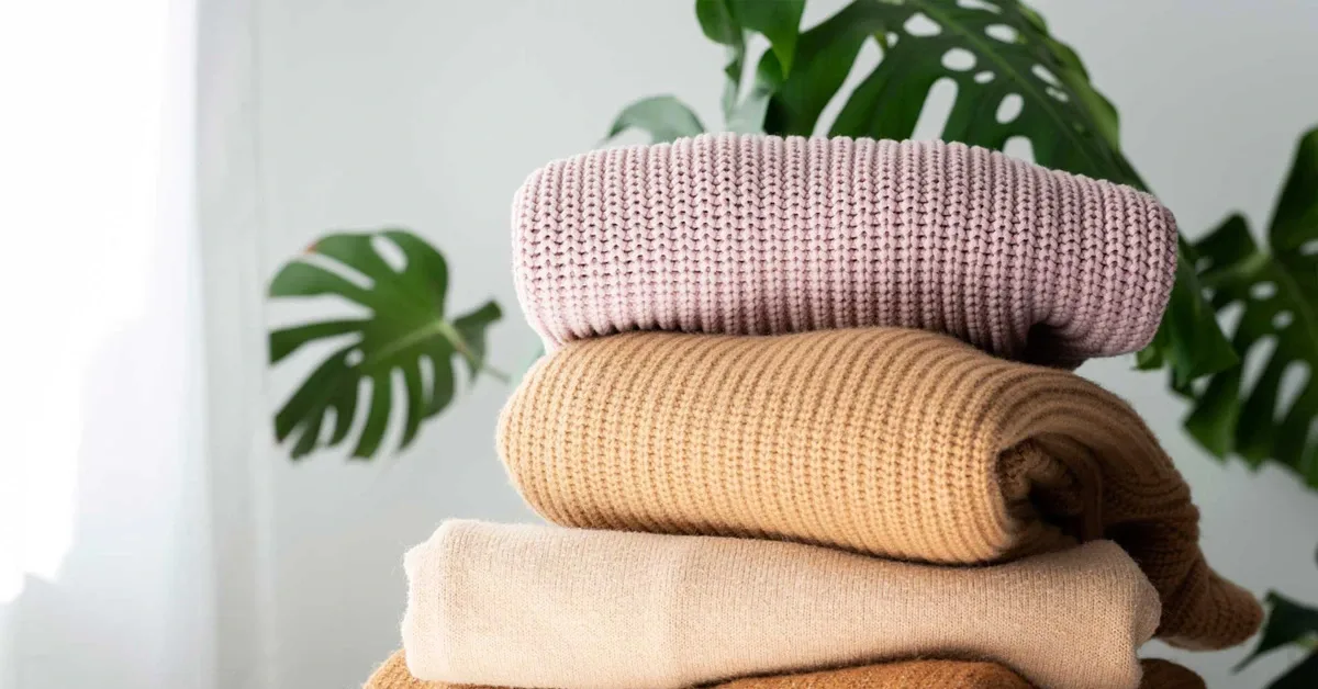 folded knit sweaters on a table with a plant in the background